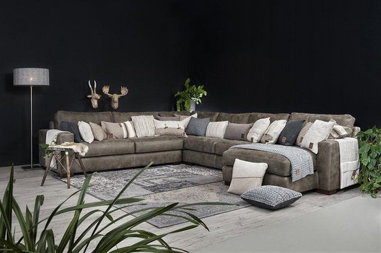Luxe hoekbank in donkerbruin leer, gedecoreerd met een veelvoud aan gebreide sierkussens en plaids.