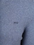 Close-up van een blauwe trui met het geborduurde logo 'MCG' op de borst.