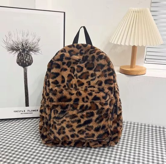 Bruine en zwarte luipaardprint, pluizige rugzak op een tafel met een geruite tafelkleed, naast een lamp en een prent.