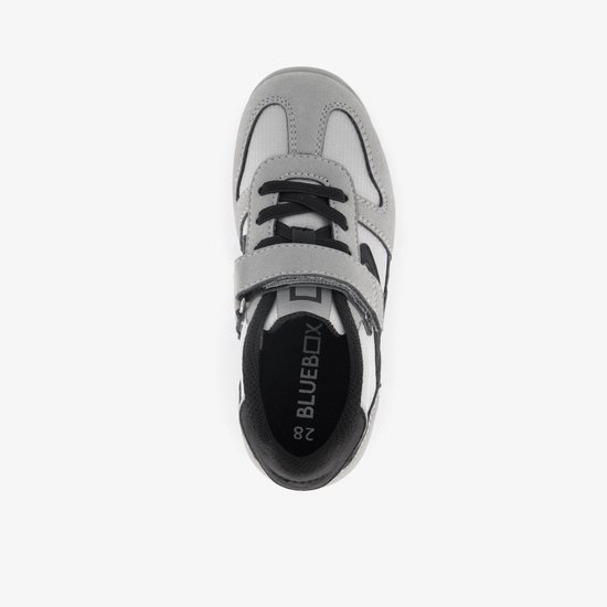 Grijze sneaker met zwarte veters, klittenbandsluiting en logo op de binnenzool.