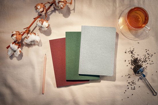 Drie Sigel Re-Up notitieboeken: rood, mosgroen en grijs, naast een tak met katoenbloesems, een potlood, thee en theebladeren.
