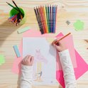 Kind tekent met oranje potlood op papier met flamingo en struisvogel.