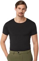 Een man met donker haar en snor draagt een zwart T-shirt en een olijfgroene broek. Hij heeft zijn hand in zijn zak.