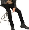 Zittend op een krukje, man met zwarte jeans met rolmouwtjes en een zwart leren jack.