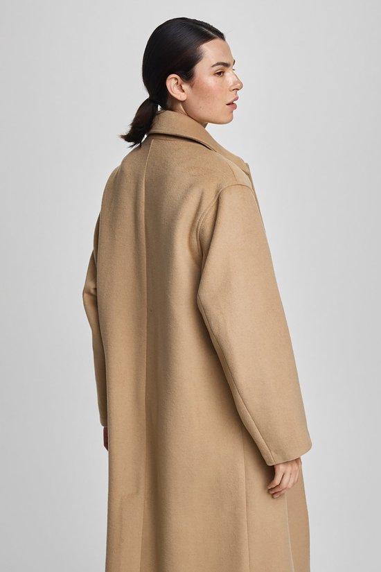 Model van achteren gezien in een lichtbruine lange jas met reverskraag, gedragen met een spijkerbroek.