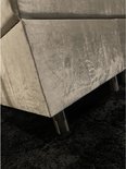 Hoekdetail van een beige velours boxspring met metalen pootjes op een zwart vloerkleed.