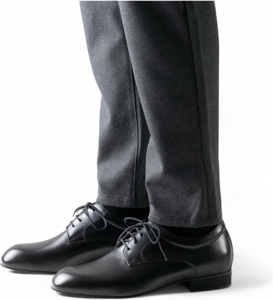 Chaussures derby noires en cuir lacées, portées par un homme en pantalon gris.