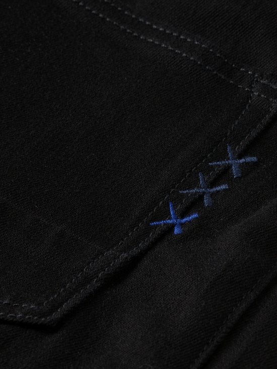 Detail van zwarte jeans met drie blauwe 'X' stiksels op de achterzak.