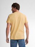 Achterkant van een man met donkergeel T-shirt en blauwe spijkerbroek.