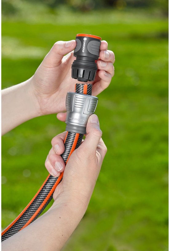 Handen bevestigen een grijze en zwarte Gardena slangkoppeling met oranje accenten aan een tuinslang.