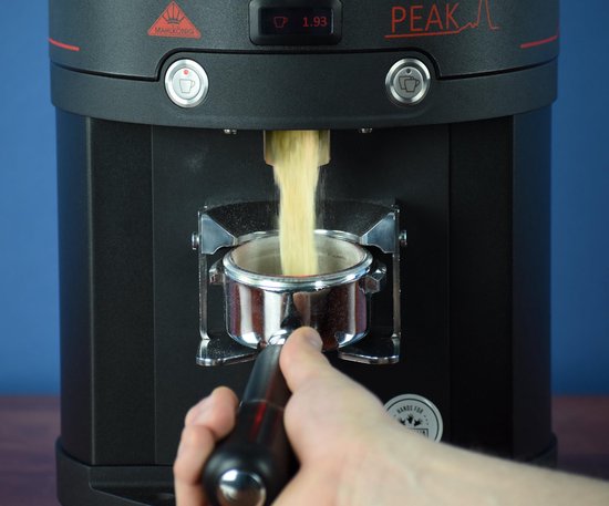 Koffie wordt gemalen uit een zwarte Peak koffiemolen in een portafilter.