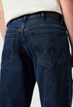 Close-up van de achterkant van een donkerblauwe spijkerbroek met Wrangler logo.