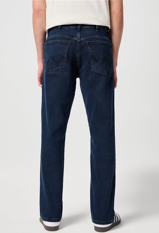 Achterkant van een man in een donkerblauwe spijkerbroek met Wrangler logo op de achterzakken.