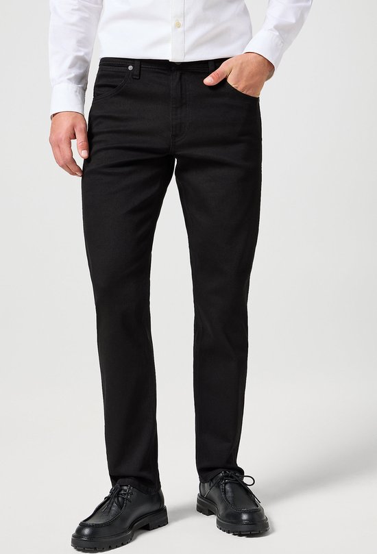 Man met een zwarte Wrangler jeans, wit overhemd en zwarte schoenen.