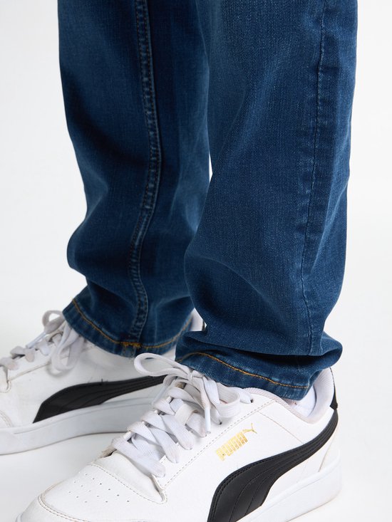 Gedetailleerde opname van de benen van een jongen in een blauwe jeans en witte sneakers.