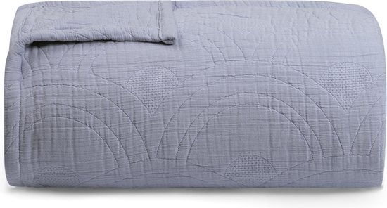 Opgevouwen lavendelblauwe mousseline spreideken met cirkelvormig stippatroon.