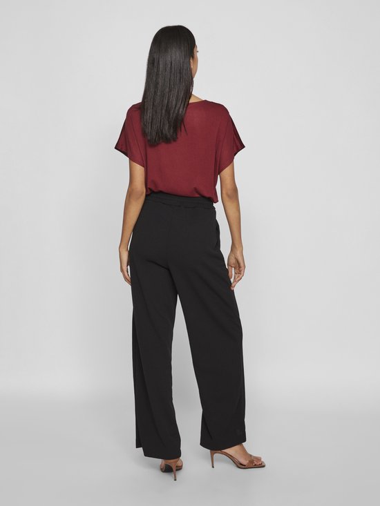 Model van achteren gezien, draagt een zwarte wijde broek en bordeauxrode top.