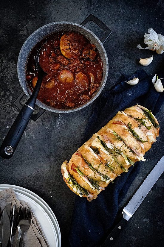Kookpot met stoofvlees en ui, naast een brood met ham en kaas. Met een handdoek en bestek.
