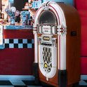 Jukebox in retrostijl met houten kast, witte en rode biezen, staand in een retro-interieur.
