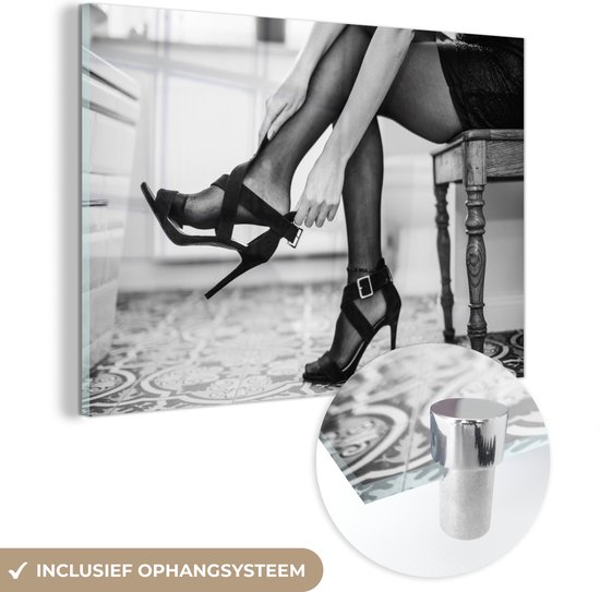 MuchoWow® Glasschilderij 120x80 cm - Schilderij acrylglas - Vrouw trekt hakken aan om te feesten - zwart wit - Foto op glas - Schilderijen