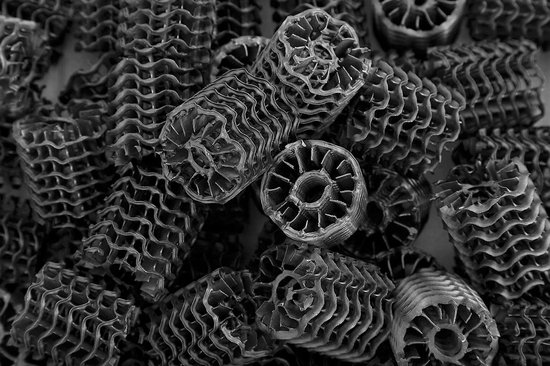 Grijze, cilindervormige Hel-X biocarrier filtermedia met golvende lamellen en een open middenkern.