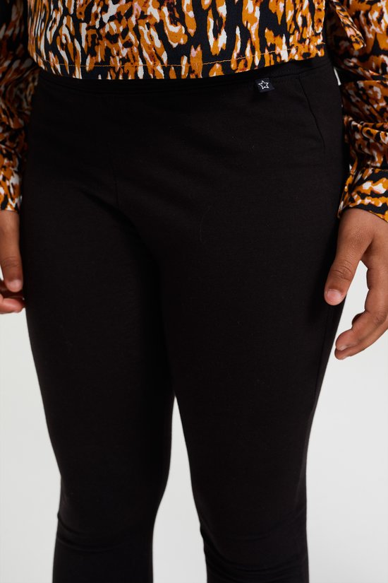 Zwarte legging met een kleine witte ster applicatie op de tailleband, gedragen onder een luipaardprint jurk.