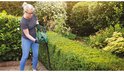 Een vrouw met veiligheidsbril en handschoenen snoeit een groene heg met een Bosch heggenschaar.