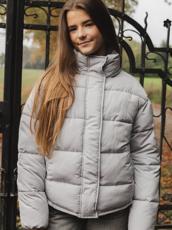 Meisje met lang bruin haar draagt grijze pufferjas met capuchon.