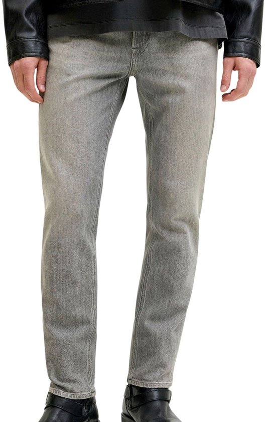 Onderlichaam van een man in een grijze jeans met steekzakken en donkere laarzen.