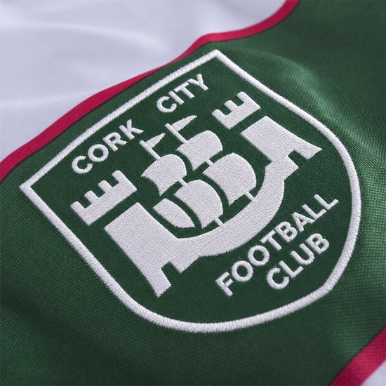 Detail van het geborduurde wapen van Cork City Football Club op een wit, groen en rood voetbalshirt.