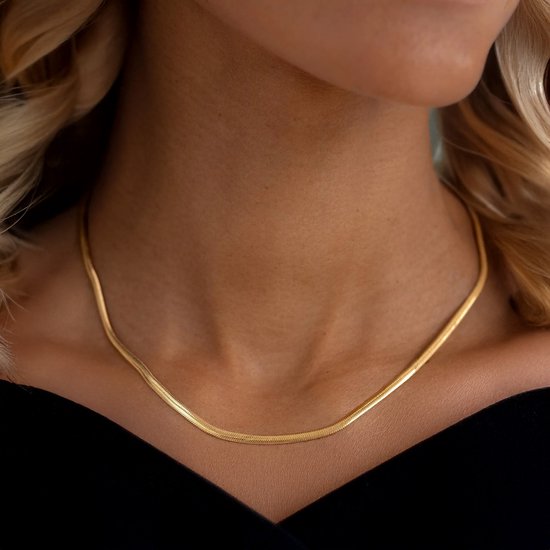 Gouden slangenketting gedragen door een vrouw, zichtbaar vanaf de schouders omhoog.
