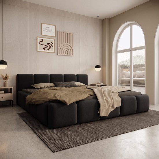 Un lit double bas en velours noir (180x200 cm) avec un matelas épais et des couvertures beiges et brunes. Une table de chevet décorée se trouve à gauche.