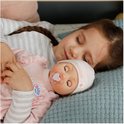 Een meisje slaapt met een baby Annabell pop in roze kleding met een fopspeen.
