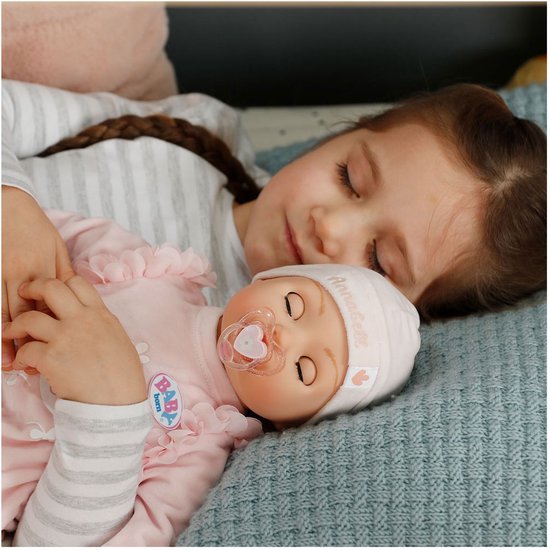 Een meisje slaapt met een baby Annabell pop in roze kleding met een fopspeen.