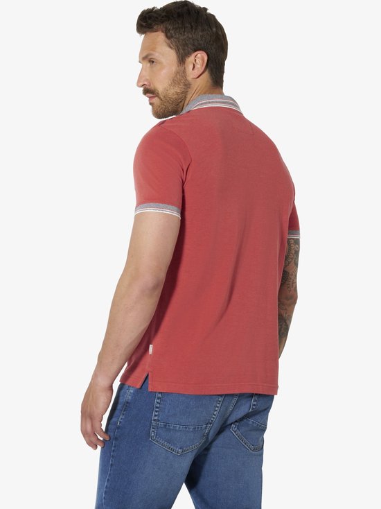 Zijaanzicht van een man in een lichtrood poloshirt met gestreepte boorden, gedragen op een blauwe jeans.
