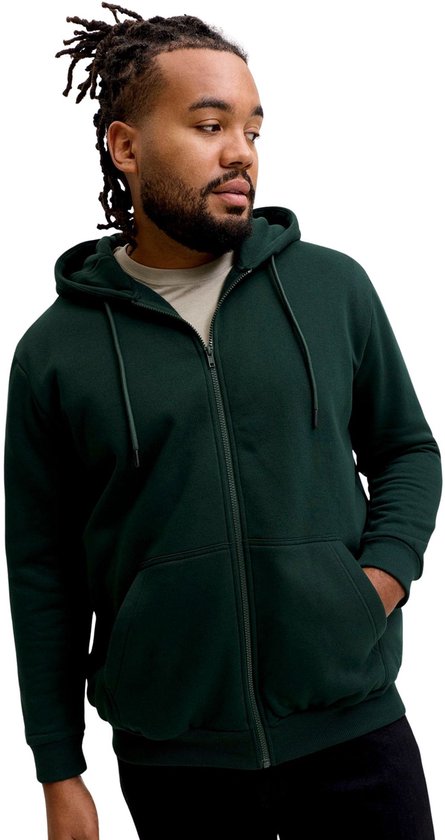 Man met dreadlocks in donkergroene hoodie met rits, beige T-shirt en zwarte broek.
