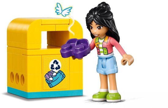 Une figurine aux cheveux tressés et taches de naissance jetant des pièces Lego violettes dans une poubelle jaune avec symbole de recyclage.