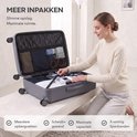 Vrouw pakt een open antracietkleurige koffer in, met interne vakken en spanbanden, in een lichte woonkamer.