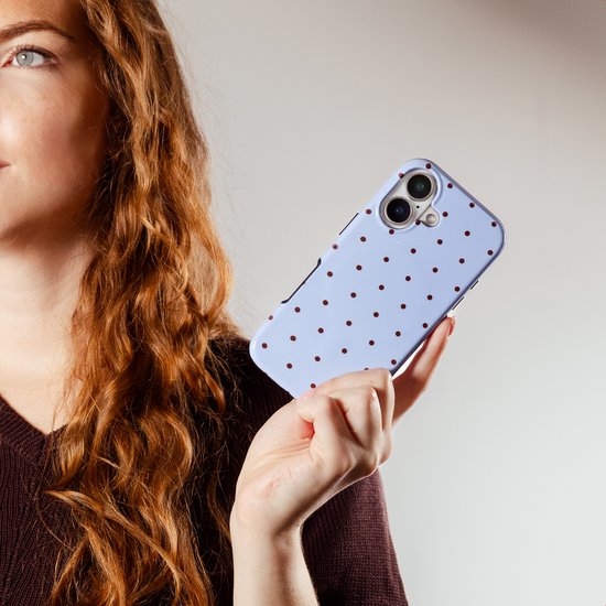 Vrouw met lang rood krullend haar houdt een lichtblauwe telefoonhoes met bruine stippen vast.