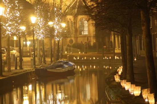 Boot in een kanaal 's nachts, omringd door lantaarns en kerstverlichting.