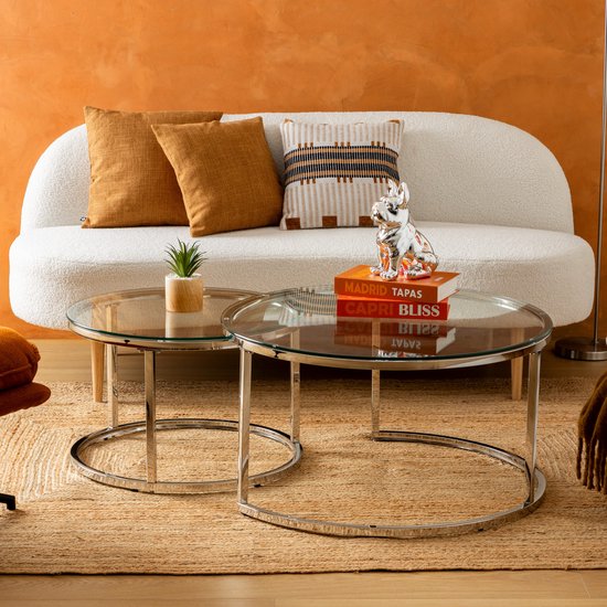 Twee ronde salontafels met glazen blad en verchroomd metalen frame in een woonkamer.