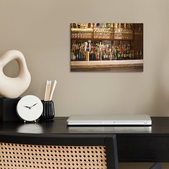 Poster met flessen drank en glazen op een bar, op een bureau met een laptop en klokje.