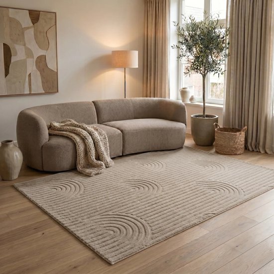 Un salon avec un canapé rond taupe et un tapis taupe avec un motif de cercles et de lignes. Une couverture tricotée est posée sur le canapé.