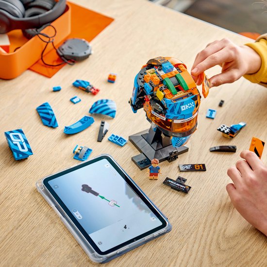 Kind bouwt LEGO McLaren F1 helm, blauw en oranje, met losse onderdelen en tablet.
