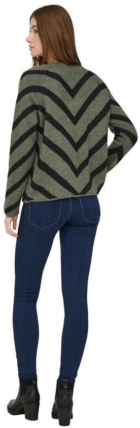 Model draagt een groene trui met zwarte chevron-strepen en donkere jeans.