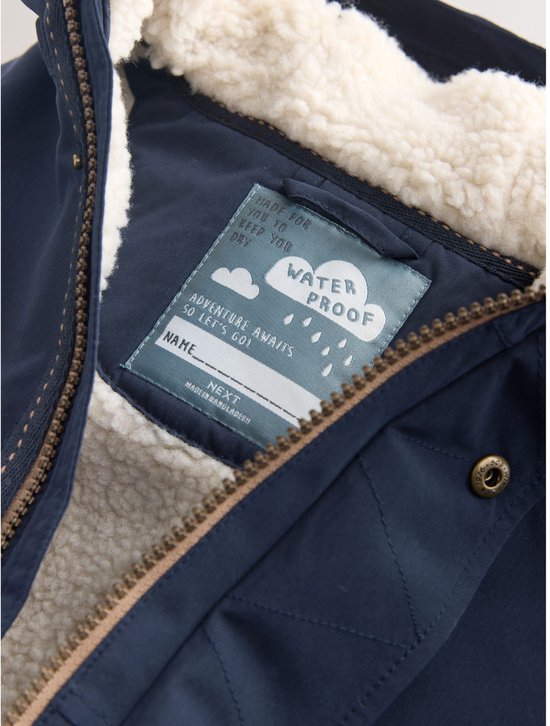 Sluiting en label van een donkerblauwe parka. Label met 'Waterproof' en plek voor naam.