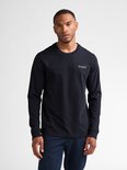 Man met donkerblauw longsleeve shirt met witte tekst op linkerborst en spijkerbroek.