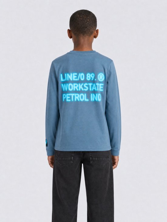 Jongen van achteren gezien, draagt een blauw longsleeve T-shirt met tekstprint op de rug.