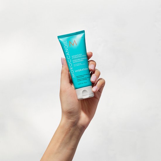 Hand met Moroccanoil Weightless Hydrating Mask tube. Turquoise met oranje M-logo en witte tekst.