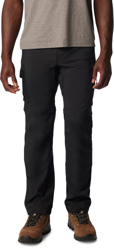 Pantalon de randonnée convertible Columbia noir pour homme, avec poches cargo et chaussures de randonnée marron.